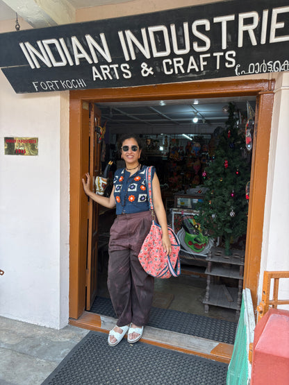 Woman standing outside a store named 'Indian Industries Arts & Crafts' with a Christmas tree inside.