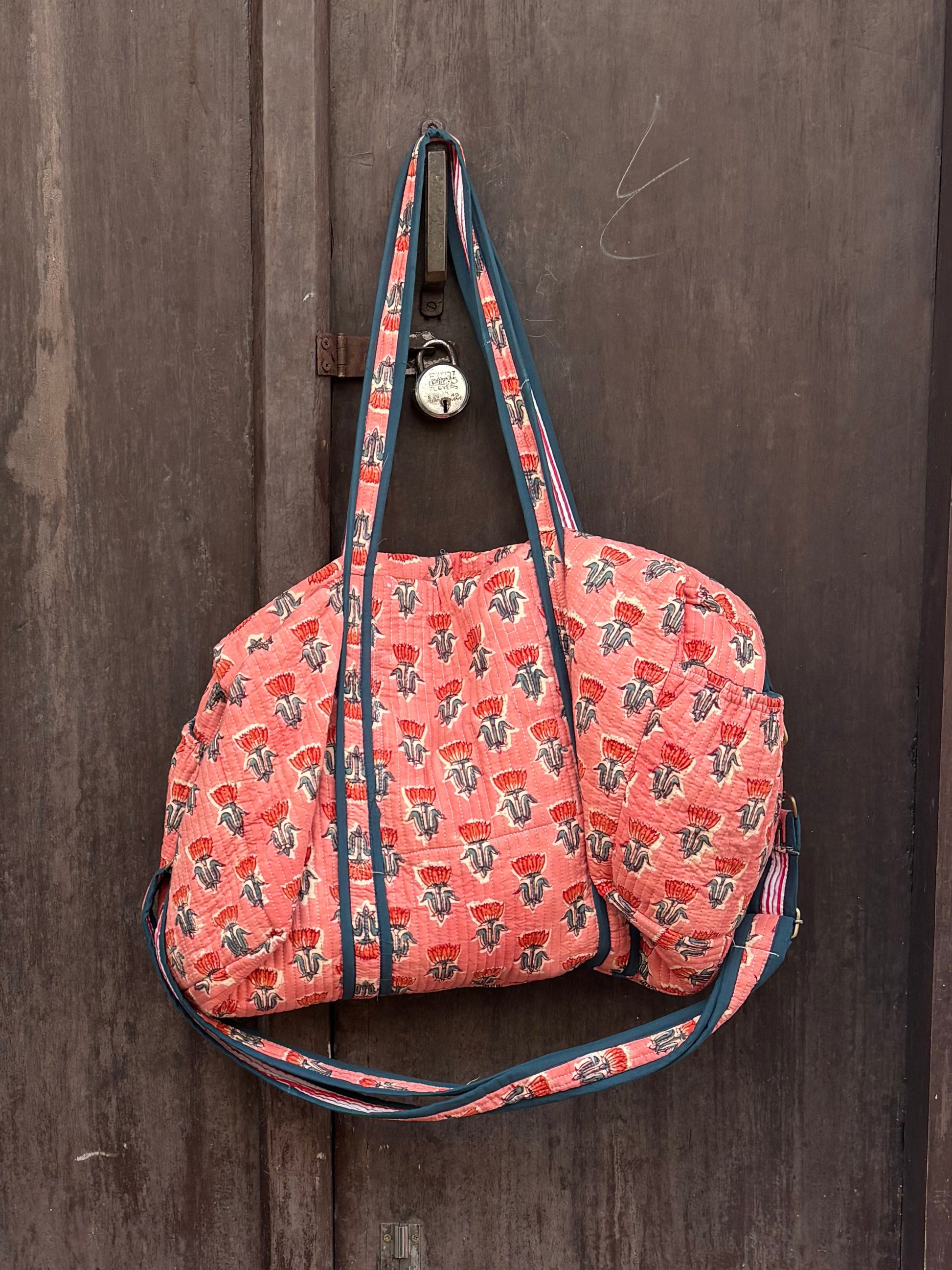 Pink floral-patterned bag hanging on a wooden door with a plant in the foreground.